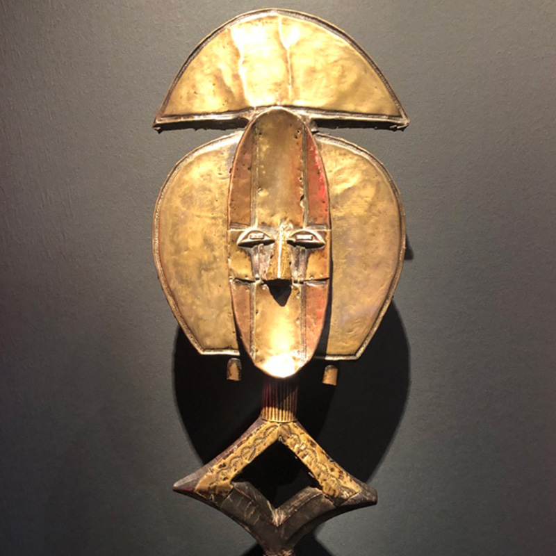 A golden African mask sculpture set against a charcoal background